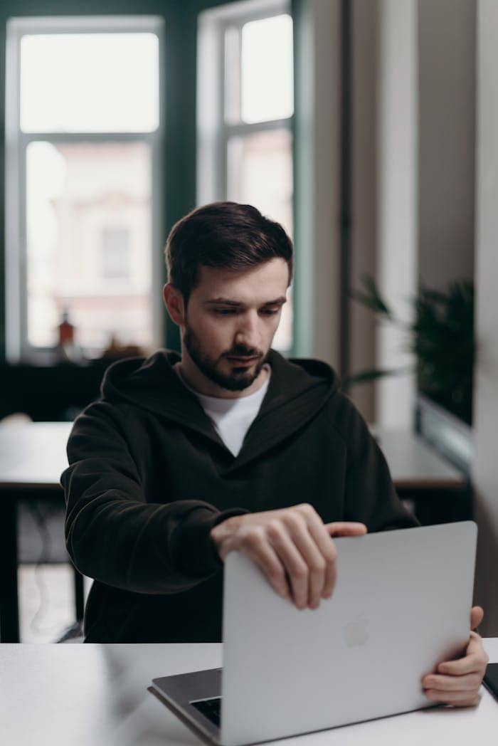 Focused young man using a laptop, working in a modern home office setting.